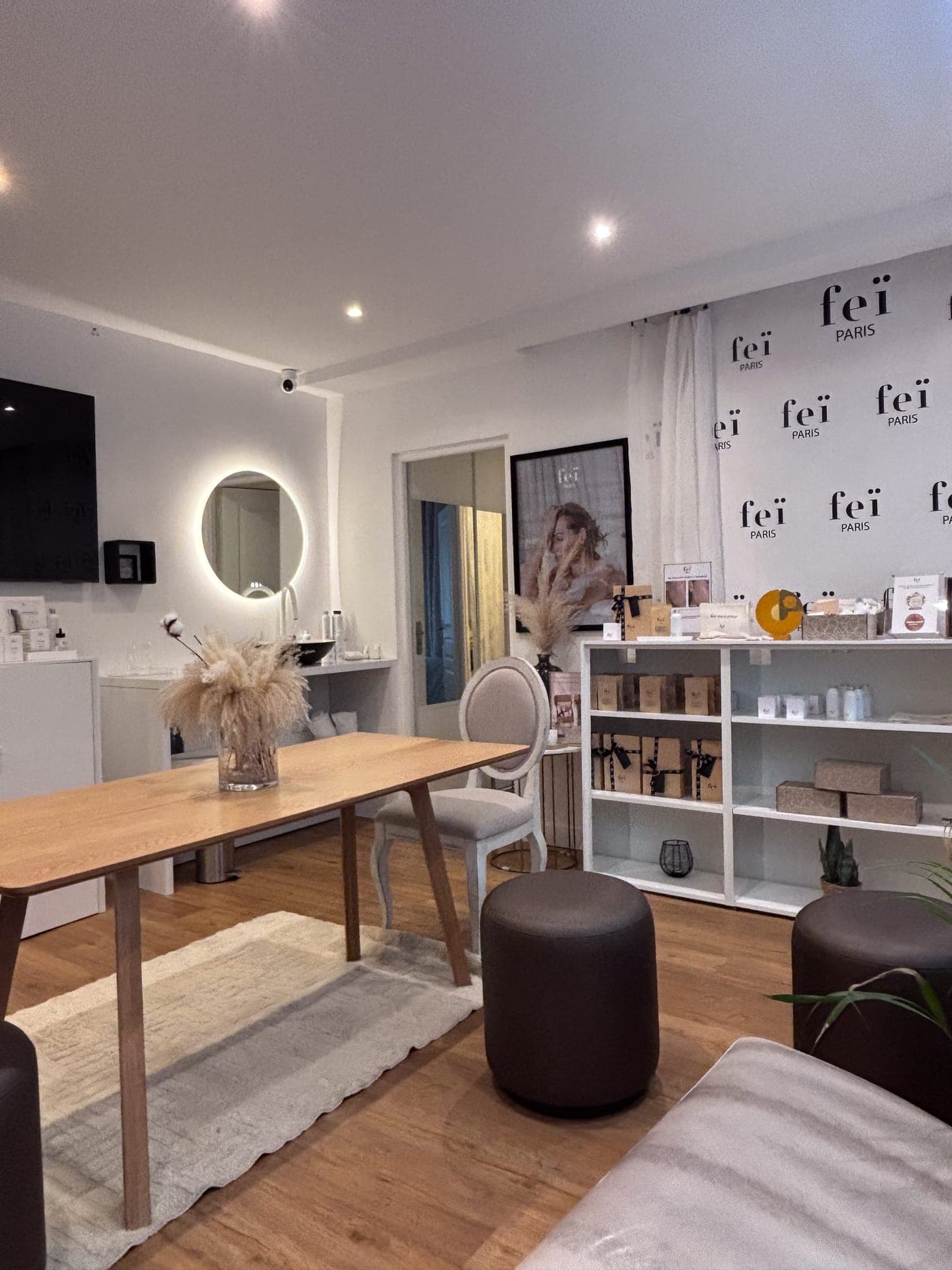 L'intérieur de la boutique Feï : grande table en bois, miroir rond lumineux et étagères de produits